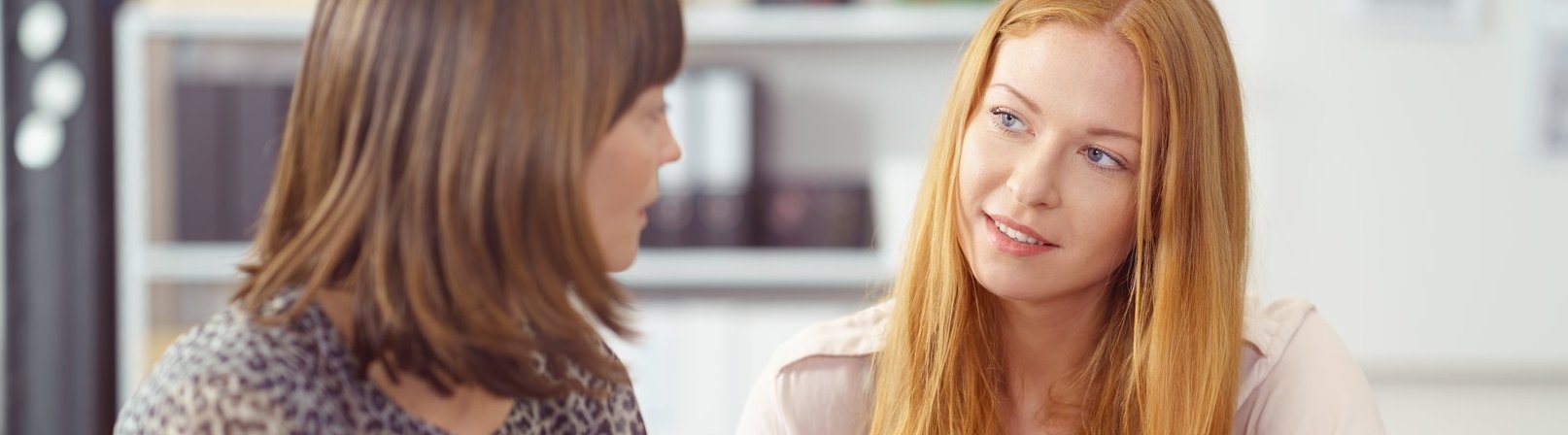 Intensive Vermittlung – von Frauen für Frauen Zwei Geschäftsfrauen in einer ernsthaften Diskussion, die gemeinsam an einem Schreibtisch sitzen und Unterlagen sichten, mit Fokus auf eine junge Rothaarige Frau.