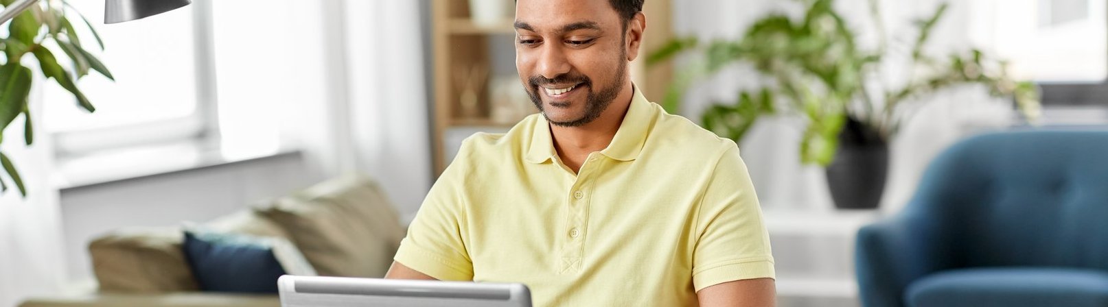 Tabellenkalkulation mit Excel Fortgeschrittene Techniken Ein glücklicher, lächelnder indischer Mann, der mit einem Laptop im Homeoffice arbeitet. Er trägt ein gelbes Hemd.