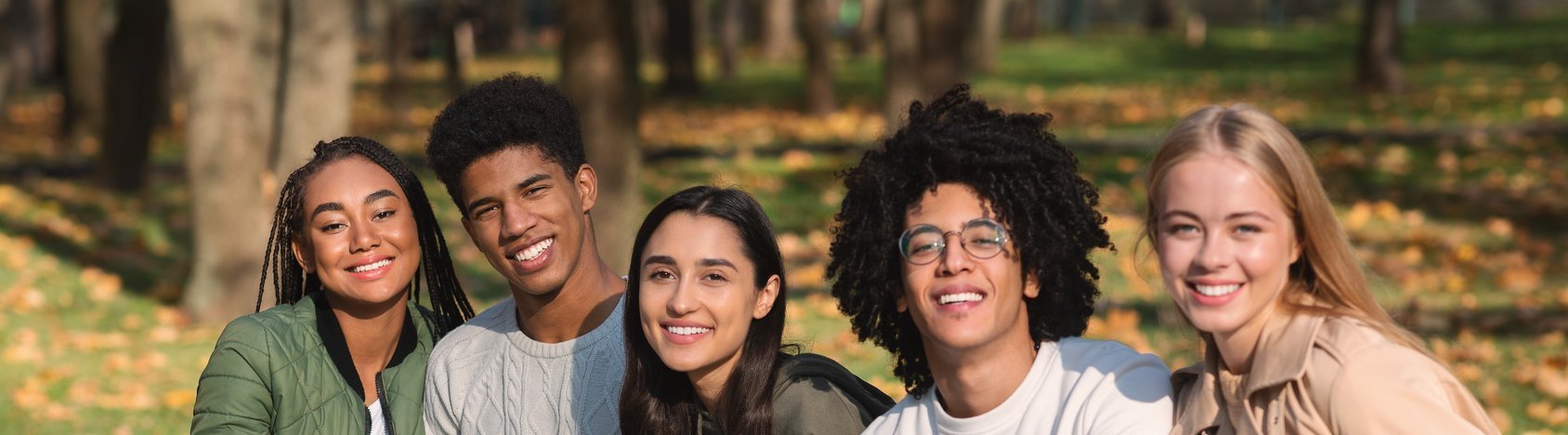 Berufseinstiegsbegleitung (BerEb) Fröhliche internationale Teenager-Freunde sitzen auf einer Bank mit ihren Geräten und verbringen Zeit zusammen im Park.